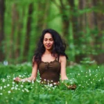 Woman meditating in a forest surrounded by green foliage