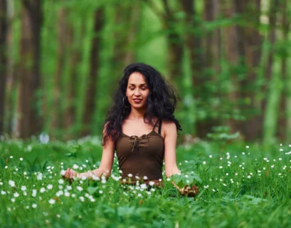 Woman meditating in a forest surrounded by green foliage