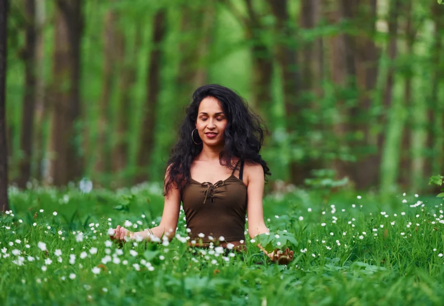 Woman meditating in a forest surrounded by green foliage