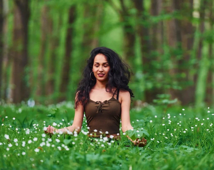 Woman meditating in a forest surrounded by green foliage