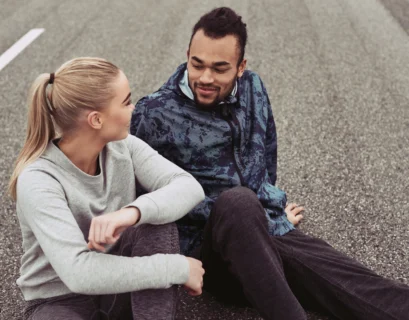 Young couple smiling while sitting on a road after jogging